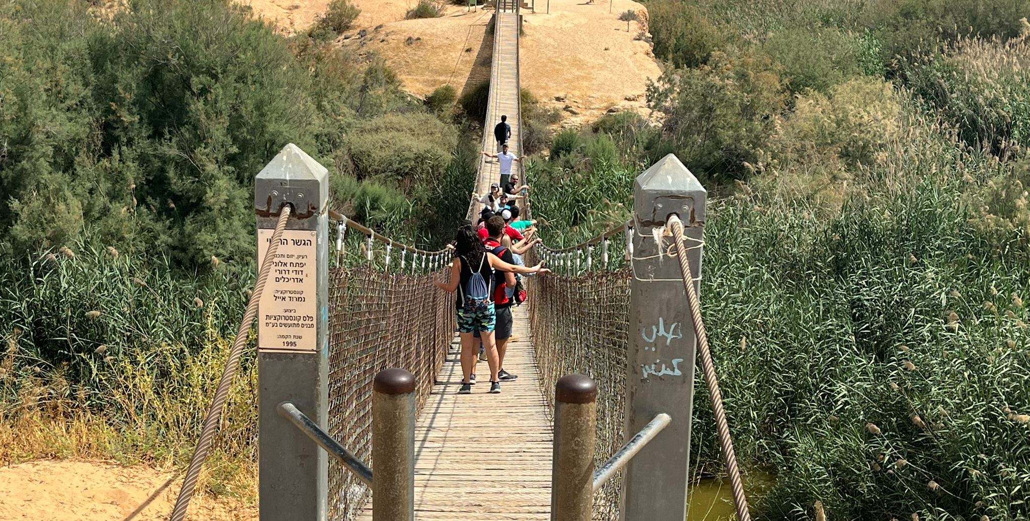 people walking narrow bridge over green valley