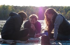 three people sitting together on a dock in front of lake